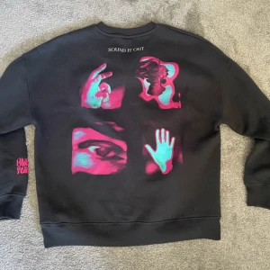 Mörkgrå sweatshirt med neontryck från Zara - Cool svart sweatshirt från Zara med unikt neonfärgat tryck i turkos och rosa på både fram- och baksida samt ärmen. Trycket har motiv av hand, öga och abstrakta former. Rund hals och ribbade muddar. Perfekt för dig som gillar statement-plagg.
