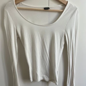 Vit långärmad topp från Gina Tricot - En enkel och stilren vit långärmad topp från Gina Tricot i storlek XS. Toppen har rund halsringning och är gjord i mjuk bomull, perfekt att matcha med jeans eller kjol för en clean look.