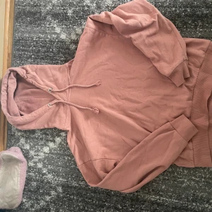 Rosa hoodie  - Mysig hoodie i dämpad rosa färg från lager 157. Tröjan har huva med snörning, ribbade muddar och lång ärm. Perfekt för chill dagar och enkel att matcha med jeans eller mjukisbyxor. Materialet är mjukt och känns skönt mot huden.