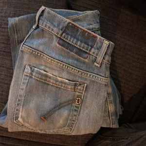 Ljusblå slitna dondups med raka ben - Snygga ljusblå jeans med slitningar på knäna och klassiska femficksdetaljer. Jeansen har raka ben och en normal passform. De är tillverkade i denim med en tvättad look och har kontrastsömmar på bakfickorna.