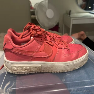 Nike Air Force 1 rosa sneakers - Nike Air Force 1 sneakers i en snygg rosa färg med matchande skosnören och vit sula. Skorna har klassisk rund tå, perforerade detaljer på tån och broderade Nike-loggor på plösen. Tillverkade i skinn och textil för en bekväm känsla. Behövs bara en lite tvätt så blir dom super fina igen! Inga hål eller något 🥰🥰