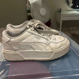 Vita sneakers från Puma, storlek 36 - Säljer ett par klassiska vita Puma sneakers i storlek 36. Skorna har en chunky platt sula, snörning och är tillverkade i skinn med textilfoder. Puma-logga på sidan och bak. Perfekta för dig som gillar en clean och sportig stil. Går att tvättas det är bara smuts. Men inga hål eller något 🥰🥰