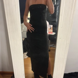 Svart axelbandslös långklänning - Säljer en svart, tight och axelbandslös långklänning med slits på sidan i storlek xs