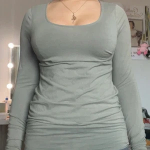 Grön långärmad topp från H&M - Säljer en enkel och stilren grön långärmad topp från H&M. Modellen har en rundad, något djupare urringning och är figurnära i passformen. Perfekt att matcha med jeans eller kjol för en clean look.