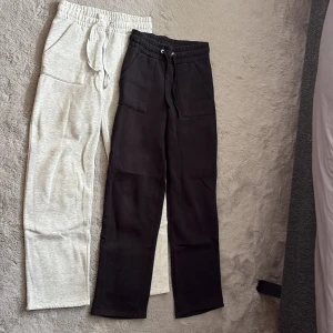 2-pack mjukisbyxor från lager 157 - Två par mjukisbyxor från lager 157 i storlek XS. Ena paret är ljusgrått och det andra svart, båda med bred resår i midjan, dragsko och stora fickor fram. Tillverkade i mjuk bomullsmix, perfekta för chill dagar eller träning.