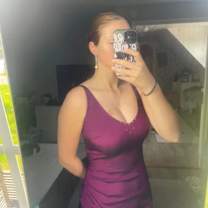Lila satinklänning med pärldetaljer - Säljer en lila, figurnära satinklänning med v-ringning och smala axelband. Klänningen har pärldetaljer vid urringningen som ger en extra touch. Perfekt för dig som vill sticka ut med en elegant och stilren look.💜🪩