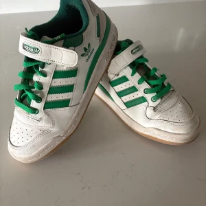 Adidas Forum  - Snygga Adidas sneakers i vitt och grönt med klassiska tre ränder på sidan, gröna skosnören och kardborreband. Skorna har perforerad tå, låg profil och gummisula. Mycket sparsamt använda! 