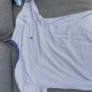 Randig t-shirt från Ralph Lauren - Snygg blå- och vitrandig t-shirt med klassisk passform. T-shirten har korta ärmar, rund halsringning med blå kant och ett broderat märke på bröstet. Perfekt för en avslappnad och stilren look.