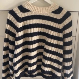 Randig stickad tröja i svart och beige - Supermysig stickad tröja med breda svarta och beige ränder. Tröjan har ribbad struktur, rund halsringning och långa ärmar. Perfekt för lager på lager och chill dagar.