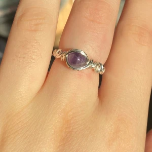 Handgjord silverring med lila sten (ametist) - Unik handgjord ring i silverfärgad metalltråd med en rund, lila sten i mitten. Snygga snirkliga detaljer runt stenen ger ringen en bohemisk vibe. Perfekt för dig som gillar personliga smycken med lite extra karaktär.