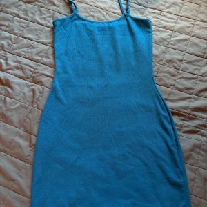 Blå ribbad klänning från NA-KD - Säljer en blå ribbad kortklänning från NA-KD med smala axelband och figurnära passform. Klänningen är stickad i mjukt material och har en enkel, stilren design som är perfekt för sommaren.