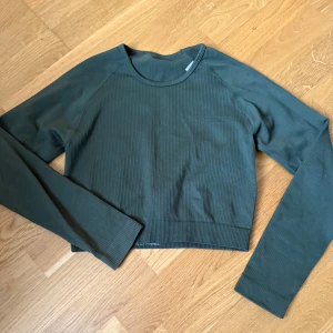 Mörkgrön ribbad croppad tröja - Snygg mörkgrön croppad tröja med ribbad struktur. Tröjan har rund halsringning och långa ärmar, perfekt för lager-på-lager. Enkel och stilren design som passar till mycket.