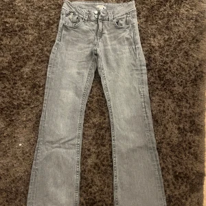Grå bootcut lowwaist jeans från Gina Tricot - Säljer ett par grå jeans från Gina Tricot i storlek 170. De har bootcut-modell med klassiska fem fickor, dubbla knappar och dragkedja. Jeansen är i ett mjukt denimtyg och har en snygg tvättad look. Perfekta för dig som gillar en avslappnad men trendig stil.
