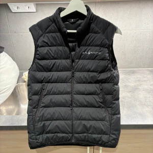 Sail Racing väst - Säljer en svart dunväst från Sail Racing i storlek XS. Västen har quiltad design, hög krage och dragkedja framtill samt två fickor med dragkedja. Perfekt för lager-på-lager och snygg logga på bröstet. Enkel och stilren look som funkar till det mesta.