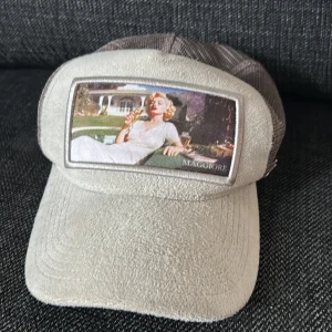 Beige keps från Maggiore med mesh - Snygg beige keps från Maggiore med mesh på sidorna och baksidan. Framsidan har en cool patch med vintageinspirerat motiv. Kepsen har en klassisk böjd skärm och detaljer i syntetmaterial. Perfekt för dig som vill sticka ut med en unik accessoar.