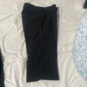 Svart kostym från Dressmann - Säljer en klassisk svart kostym från Dressmann. Kostymen består av en stilren kavaj med två knappar och matchande kostymbyxor. Tidlös design med slät yta och diskreta detaljer, perfekt för dig som vill ha en clean och snygg look. Helt ny pris kan diskuteras!