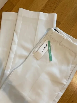 Vita straight byxor från Gina Tricot - Snygga vita byxor från Gina Tricot i rak modell med normal passform. Byxorna har klassiska fickor och hällor för bälte. Perfekta för dig som gillar stilrena och fräscha looks. Materialet är mjukt och känns bekvämt mot huden.