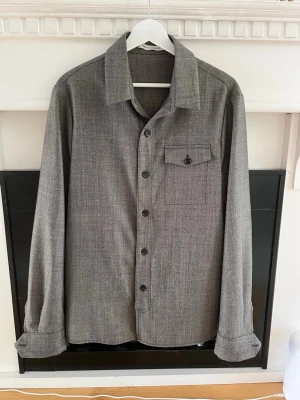 Grå overshirt från Alster Vandel - Snygg grå overshirt från Alster Vandel i storlek 48. Jackan har klassisk krage, knappstängning framtill och en bröstficka med lock. Materialet är 80% ull och 20% polyester med mjuk polyesterfoder. Perfekt för lager-på-lager och chill stil. Kan mötas upp u Stockholms området