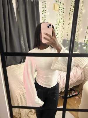 Vit långärmad topp med vida ärmar - Säljer en vit långärmad topp med riktigt vida ärmar och rund hals. Toppen har en slim passform och är tillverkad i ett mjukt bomullsmaterial. Perfekt för dig som gillar minimalistisk stil med en twist på ärmarna.