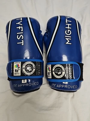 Mightyfist taekwondo skydd - Säljer ett par blåa mightyfist taekwondo sparringskydd i storlek S. Knappt använda men har små defekter som färg från andra handskar som kan ses på bilderna.