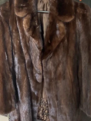 Brun pälsjacka med spetsdetaljer - Säljer en brun mink pälsjacka med bred krage och lyxig känsla. Insidan är fodrad med brunt satin och har snygga svarta spetsdetaljer längs kanten. Perfekt för dig som vill sticka ut med en elegant och unik jacka.