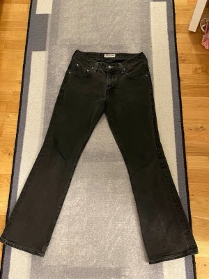 Svarta (mörkgrå) bootcut jeans från Lee -  Jeans från Lee med klassisk femficksdesign och bootcut-ben. Perfekt för dig som gillar retrovibbar och vill ha ett par coola svarta jeans.