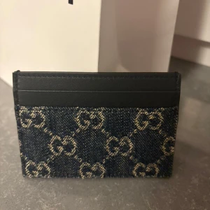 Äkta Gucci blå plånbok i denim och skinn - Säljer en snygg plånbok från Gucci med klassiskt GG-mönster i blå denim och svarta skinnpartier. Perfekt för kort och sedlar, stilren och lätt att ha med sig. Ikonisk design som sticker ut i vardagen.