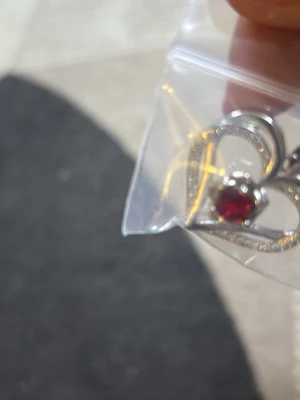 Halsband med hjärthänge i silverfärg och guld färg - Säljer ett halsband med ett glittrigt hjärthänge i silverfärg. Hänget har en gnistrande sten i mitten och är dekorerat med små stenar runt om. Kedjan är tunn och elegant, perfekt för att ge en söt touch till din outfit.