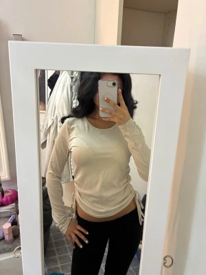 Beige ribbad långärmad topp - Säljer en beige långärmad topp med ribbad struktur och snörning i sidorna. 