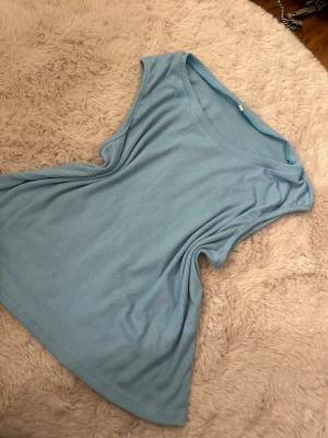 Ljusblå ribbad linnetopp - Snygg ljusblå ribbad linnetopp med rund halsringning och ärmlös design. Perfekt för varma dagar och enkel att matcha med jeans eller kjol. Mjuk och stretchig känsla i materialet.