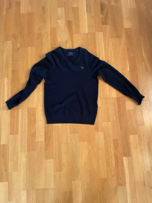 Mörkblå v-ringad tröja från GANT - Snygg mörkblå v-ringad tröja från GANT i extra fin lammull. Tröjan har lång ärm, ribbade muddar och en diskret logga broderad på bröstet. Perfekt för dig som gillar klassisk och stilren design med mjukt material.