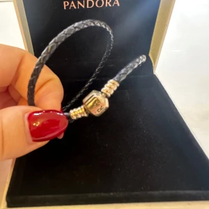 Mörkblå flätad skinnarmband från Pandora - Säljer ett mörkblått flätad armband från Pandora med snygga guldfärgade detaljer och lås. Den har aldrig använts men suttit i garderoben ett par år.  