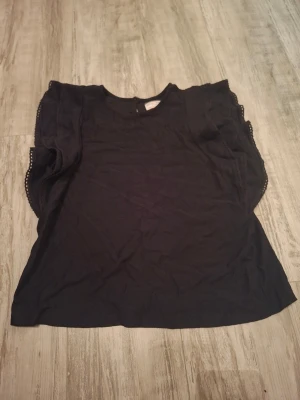 Svart blus med volangärmar - Säljer en svart blus från Lindex (Holly & white)  volangärmar och spetskant längs ärmarna. Storlek S. Andvänd ungefär 2 gånger och är i fint skick, inget hål eller fläck. Vet ej vad jag köpt den för då det var några år sedan, priset kan förhandlas!