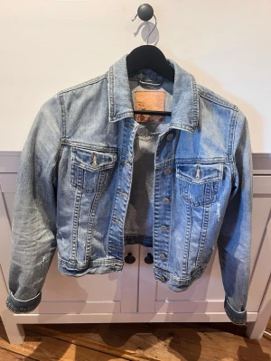 Ljusblå jeansjacka med knappar - Säljer en klassisk ljusblå jeansjacka med silverfärgade knappar och två bröstfickor med knapp. Skulle säga passar xs men är i storlek S. Sitter tight på mig som är S. 