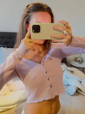 Ljuslila croppad kofta  - Superfin ljuslila croppad kofta med ribbad struktur och snygga bruna knappar framtill. Perfekt att styla med jeans eller kjol.