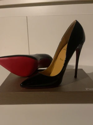 Svarta Christian Louboutin klackar  - Säljer ett par ikoniska svarta klackar  från Christian Louboutin med glansig finish och klassisk röd sula. Skorna har spetsig tå och hög klack, tillverkade i skinn. Perfekta för dig som vill ha en lyxig och edgy look.