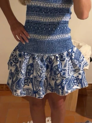 Blåvit kortklänning med volang - Säljer en superfin blåvit kortklänning med smockad överdel och volangig kjol. Perfekt för sommarens alla tillfällen!