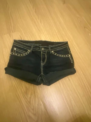 Svarta jeansshorts med nitar - Snygga svarta jeansshorts med kontrasterande ljusa sömmar och coola nitar på fickorna. Shortsen har uppvikta ben och detaljerade knappar på bakfickorna. Perfekta för dig som gillar lite extra bling och streetstyle. Pris kan diskuteras!!!