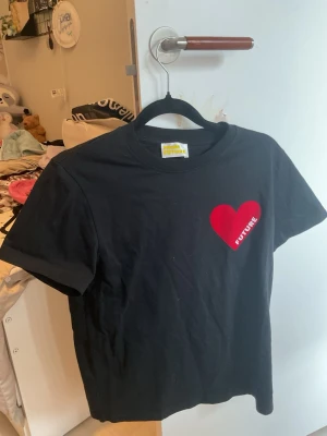 Svart t-shirt från From Future - Svart t-shirt från From Future med ett stort rött hjärta och texten 'FUTURE' tryckt på bröstet. Klassisk rund hals och korta ärmar. Materialet är mjuk bomull som känns skönt mot huden. Perfekt för dig som gillar grafiska prints och vill sticka ut lite extra.