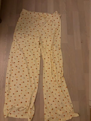 Gula mjukisbyxor med apelsinmönster - Säljer ett par ljusgula mjukisbyxor från Holly Printed i storlek M. Byxorna har ett gulligt apelsinmönster över hela tyget och snörning i midjan för extra komfort. De är vida i modellen och gjorda i mjukt bomullsmaterial. Oanvända 