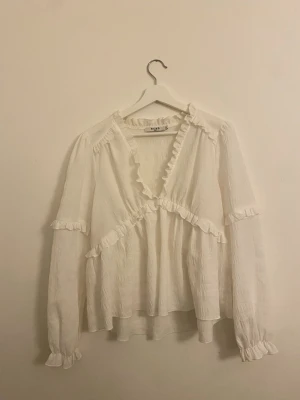 Vit volangblus från NA-KD – strl S - Säljer en vit, feminin blus från NA-KD med v-ringning och fina volangdetaljer. Blusen har lång ärm med resår vid ärmsluten och en luftig, lätt transparent kvalitet som ger ett elegant fall. Blusen är använd men i bra skick. Passar perfekt både till vardag och mer uppklädda tillfällen.