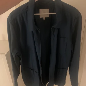 Blå overshirt från Pepe Jeans - Snygg blå overshirt från Pepe Jeans med dragkedja framtill, klassisk krage och bröstficka. Långärmad modell i bomull som passar perfekt till lager-på-lager. Diskret logga på ärmen och stilren design.