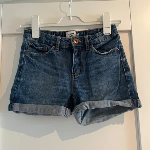 Blå jeansshorts från 157, storlek 160 - Snygga blå jeansshorts från 157 i klassisk femficksmodell med uppvikta benslut. Shortsen har normal passform, knapp och dragkedja framtill samt resår baktill i midjan. 