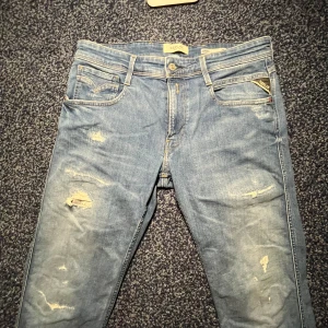 Replay Anbass med slitningar  - Säljer ett par Replay Anbass jeans i ljusblå tvätt med slitningar och trasiga detaljer på benen. Slim fit-modell. Dom är näst intill nyskick. Har inte använt dom för dom är lite stora för mig. Lägg gärna bud! 