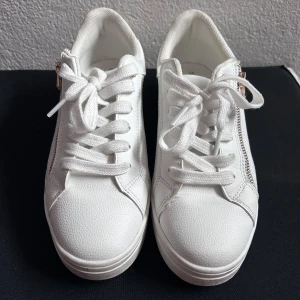 Vita sneakers med gulddetalj och dragkedja - Snygga vita sneakers med gulddetalj på hälen och dragkedja i sidan. 