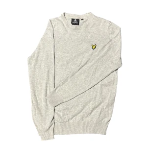Ljusgrå tröja från Lyle & Scott - Ljusgrå stickad tröja från Lyle & Scott med rund halsringning och klassisk gul logga på bröstet. Sitter relativt slim fit. Helt felfri.