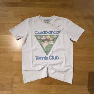 Vit Casablanca Tennis Club t-shirt - Vit t-shirt från Casablanca. Klassisk rund hals och korta ärmar. Tillverkad i 100% ekologisk bomull för en mjuk och skön känsla. Perfekt för dig som gillar sportig och stilren design.