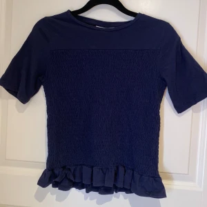 Marinblå topp med volang  - Supersöt mörkblå topp från Gina Tricot med smockad framsida och volangdetalj längst ner.☺️☺️