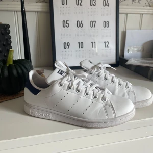 Adidas Stan Smith vita sneakers - Klassiska Adidas Stan Smith sneakers i storlek 36,5 vitt med mörkblå detalj, har använts bara några gånger av test fall säljer på grund av jag kan inte ha skor pg av skada så bara testat skorna nån gång, man ser på dem sista bilderna vart dem är lite repiga och så, köpte nypris på zalando runt 800 kr, skriv vid minsta fundering pris går oftas alltid att diskutera❣️ 