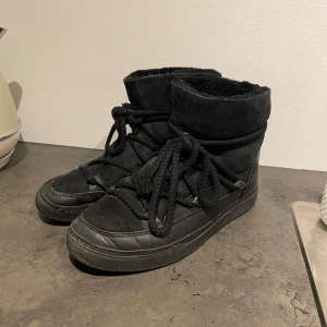 Svarta Inuikii skor - Säljer dessa äkta svarta inuikki vinterskor! Så bra till vintern. Storlek 37 men passar mig jättebra som brukar ha 38-39. Helt äkta men lite tecken på användning därav det låga priset. Skorna har snörning och platt sula. Skorna är fodrade och har en ovandel i mocka och detaljer i skinn. Perfekta för kalla dagar med sin varma insida och coola look. Klassisk rund tå och grova snören ger en unik stil.
